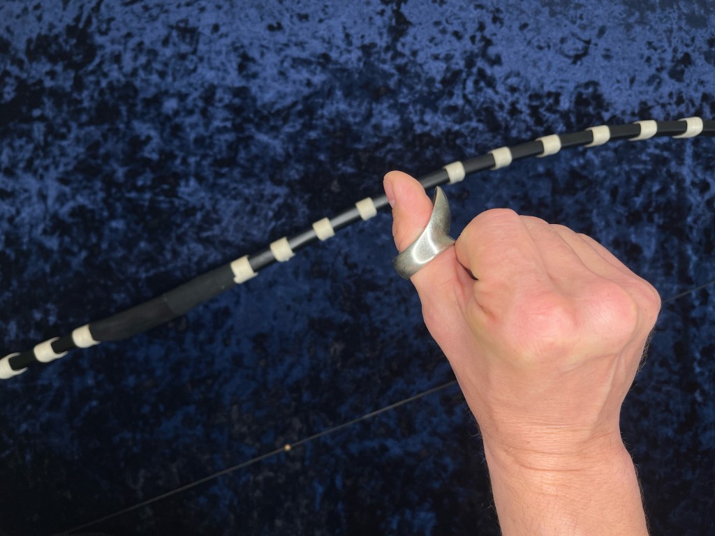 Deep hook thumb ring on a thumb with a yumi bow in the background.