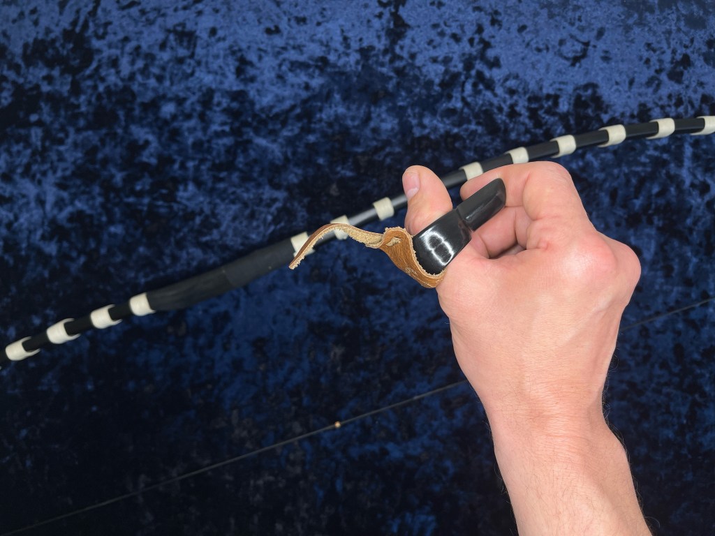 Sugakji Korean archery  thumb ring on a thumb with a yumi bow in the background.